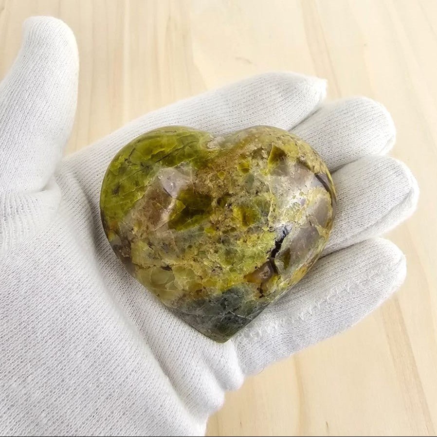 Green opal back view heart shape in gloved hand