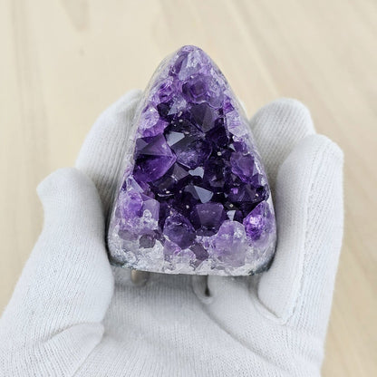 Amethyst crystal held by a gloved hand on a beige background