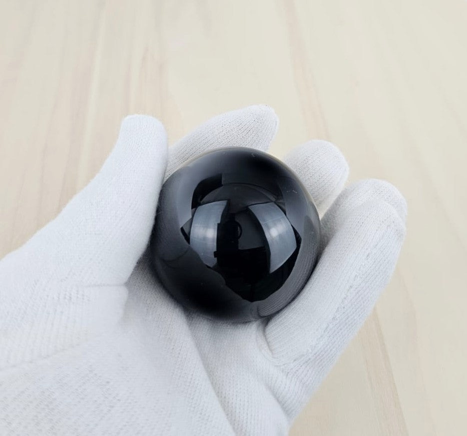 Black obsidian held in a gloved hand on a light wooden surface