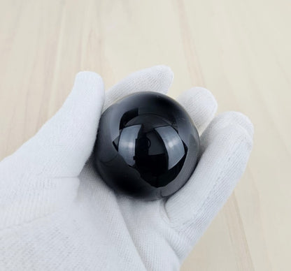 Black obsidian held in a gloved hand on a light wooden surface