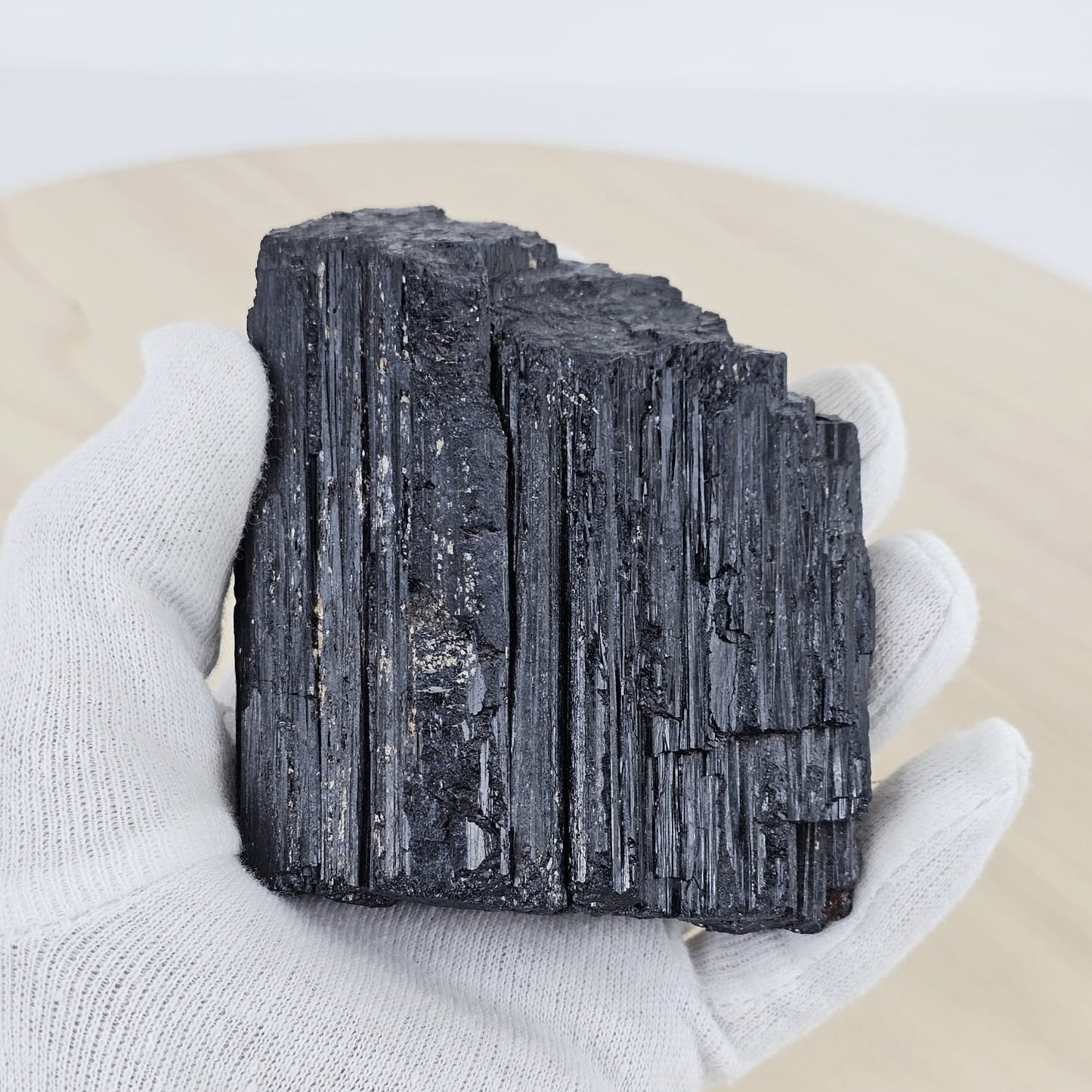 Stack of black tourmaline crystals held by a gloved hand on a beige surface