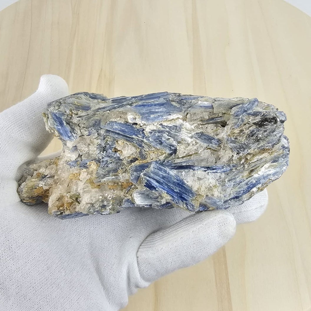 Blue kyanite in matrix held by a gloved hand on a wooden surface