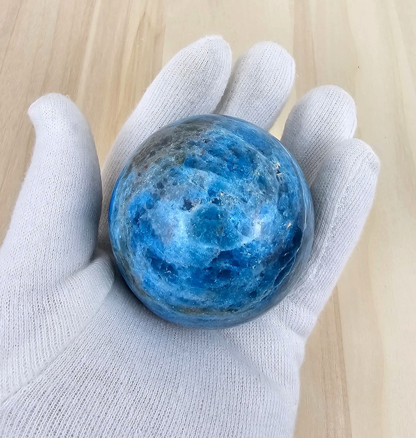 Blue apatite held in a white glove on a light wooden surface
