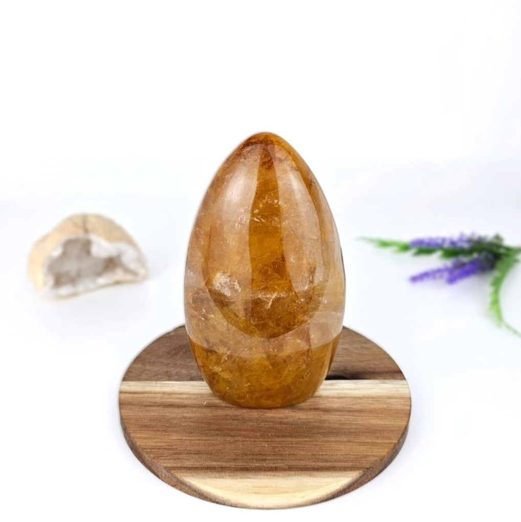 Golden healer freeform crystal on a wooden stand with a white background