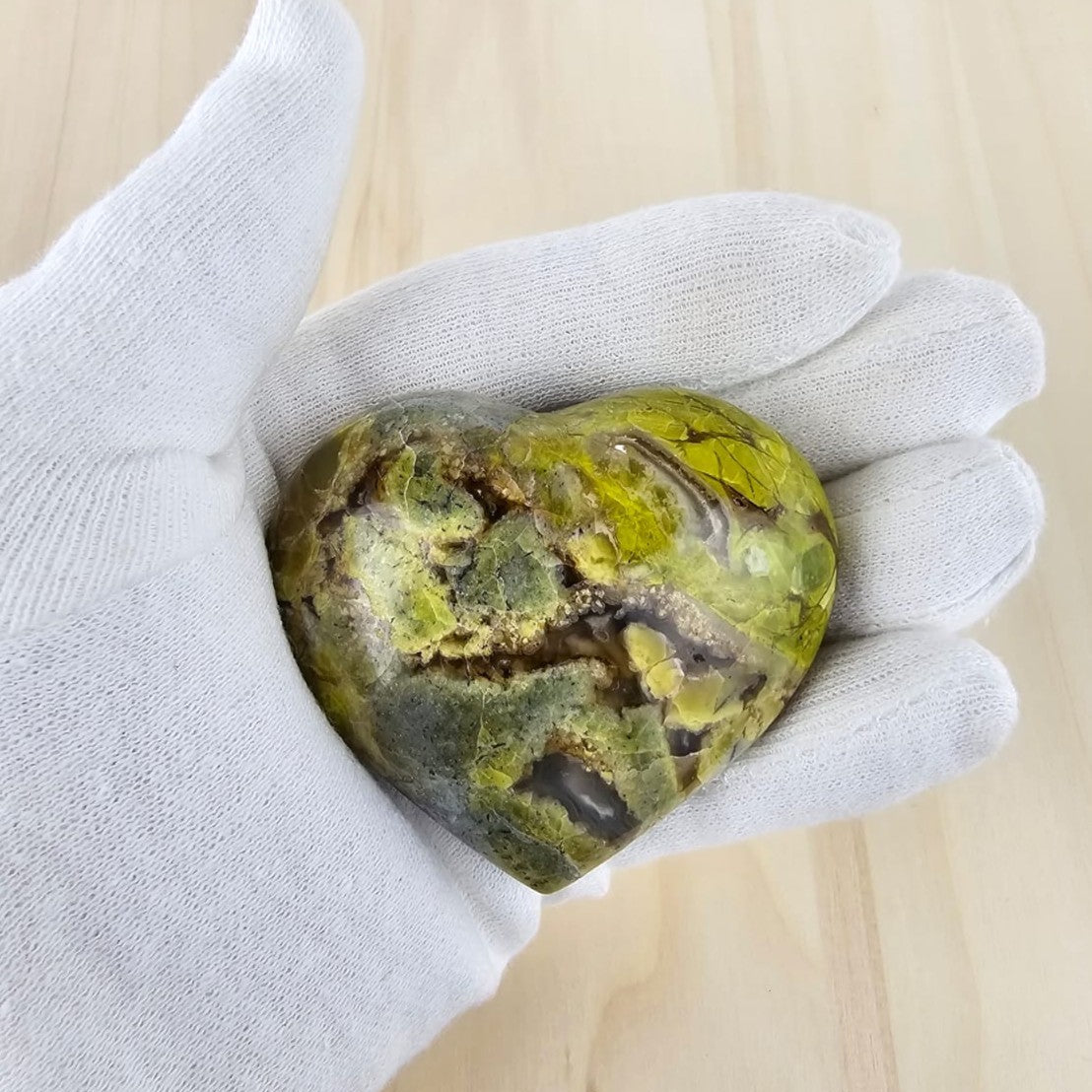 Heart-shaped green opal held in a white glove on a light wooden background