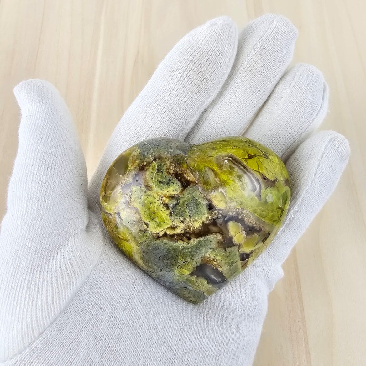 Heart-shaped green opal held in a white glove on a light wooden background