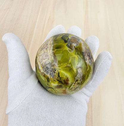 Green opal held in a white gloved hand on a wooden surface
