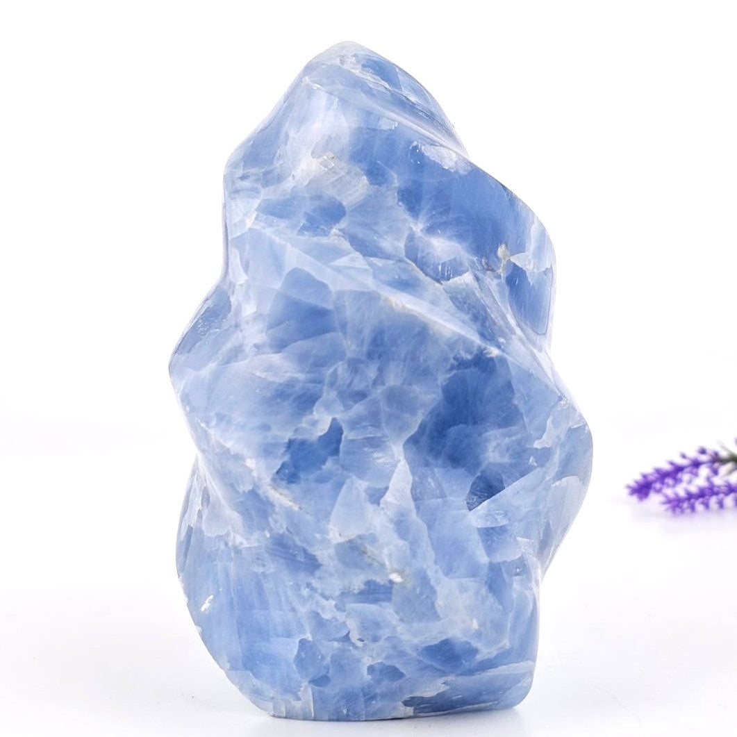 Blue calcite flame sculpture crystal rock with a small purple flower on a white background