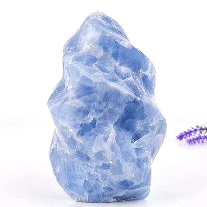 Blue calcite flame sculpture crystal rock with a small purple flower on a white background