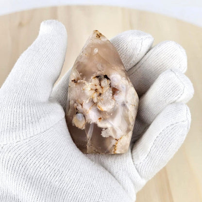 Flower agate flame sculpture held in a white glove on a light background