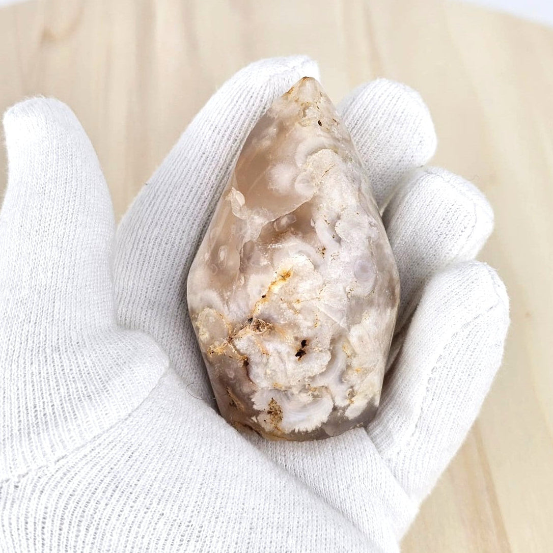 Flower agate flame sculpture held in a white glove on a light background