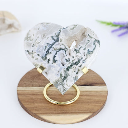 Heart-shaped moss agate on a wooden stand with a blurred background