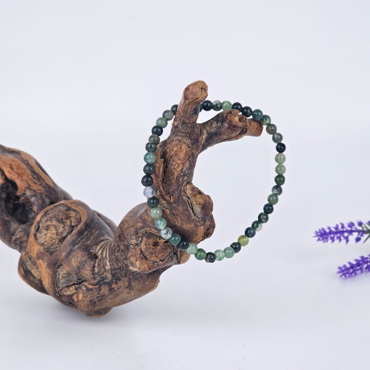 Moss agate beaded bracelet on a wooden branch with a blurred purple flower in the background