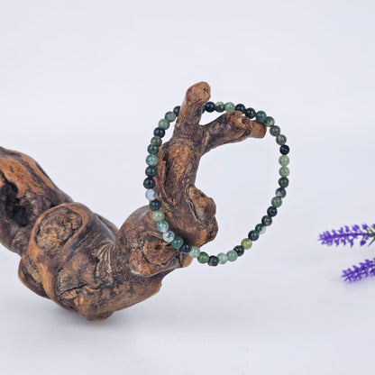 Moss agate beaded bracelet on a wooden branch with a blurred purple flower in the background