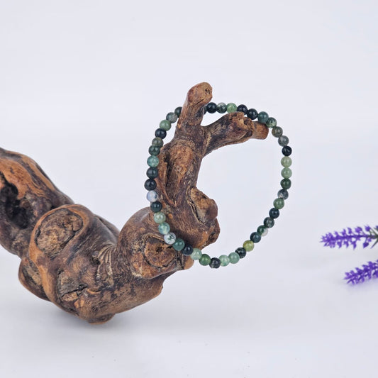 Moss agate beaded bracelet on a wooden branch with a blurred purple flower in the background