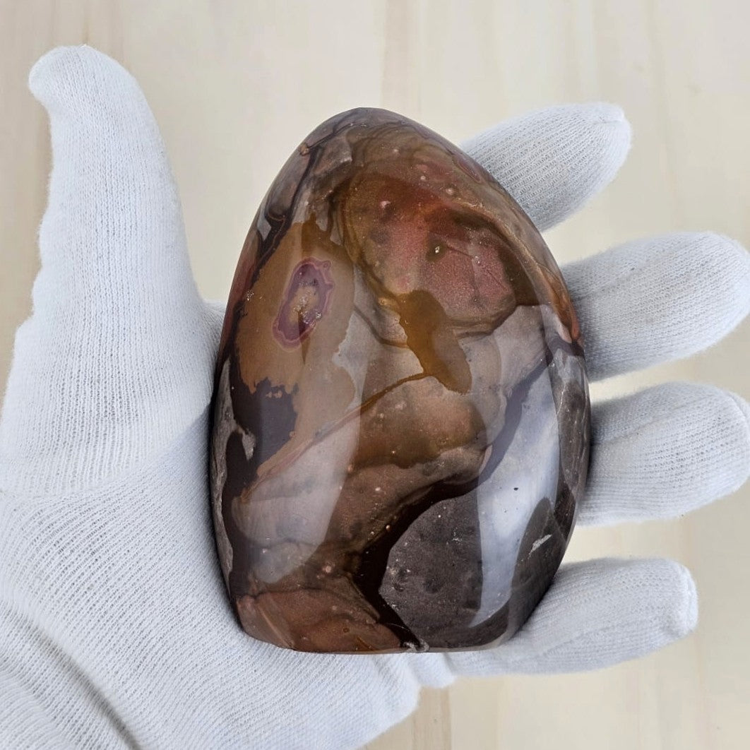 Polished polychrome jasper held in a white glove against a beige background