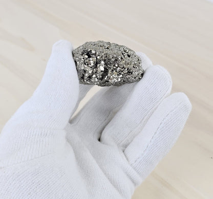 Pyrite stone held by a gloved hand on a neutral background