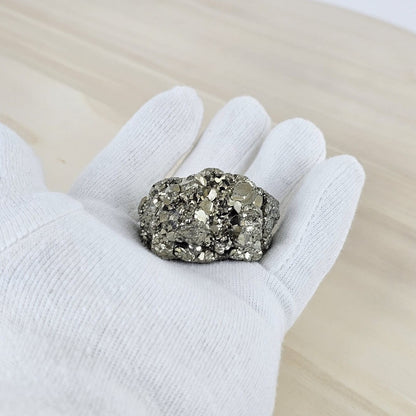 Pyrite held in a white glove on a light wooden surface