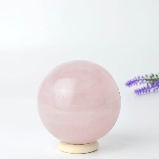rose quartz sphere on a white background with purple flowers in the corner