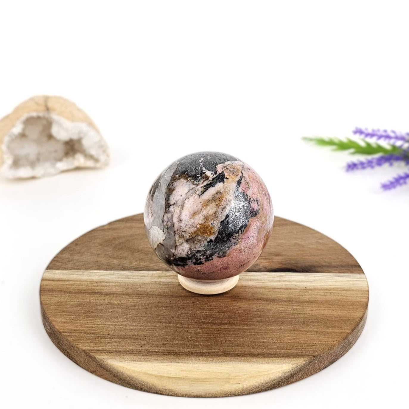 Rhodonite crystal sphere on a wooden plate with a white background