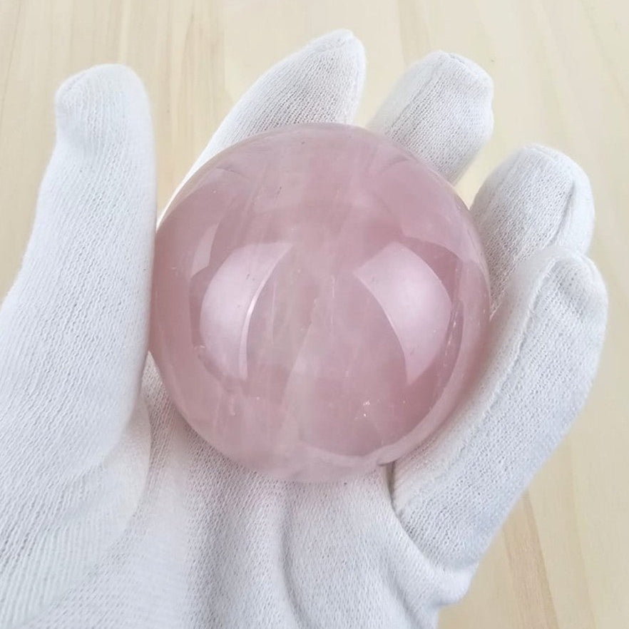 rose quartz crystal sphere held by a white gloved hand on a light wooden background