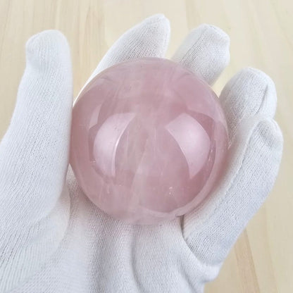 rose quartz crystal sphere held by a white gloved hand on a light wooden background