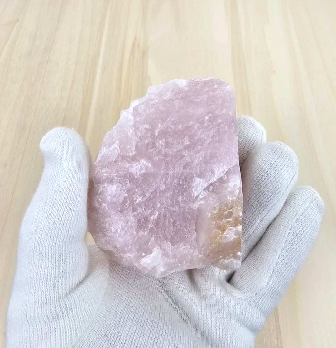 Rose quartz held by a gloved hand on a light wooden surface