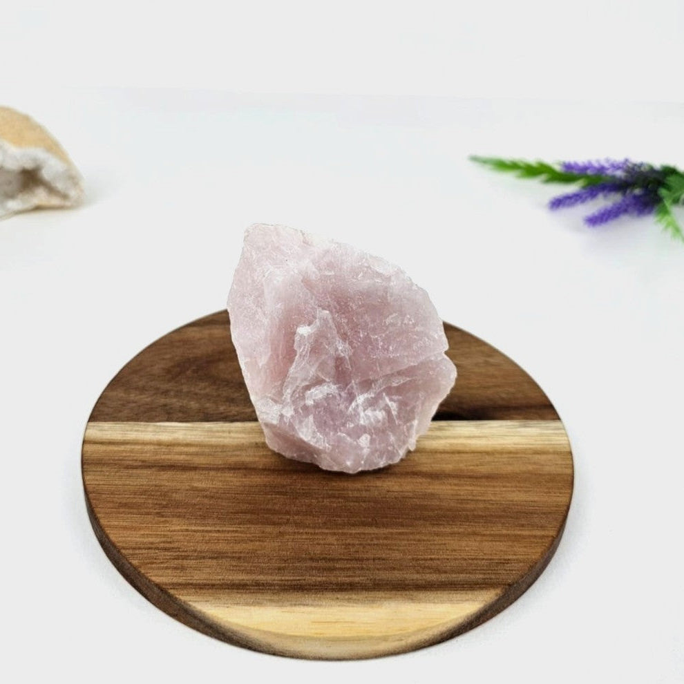 Raw pink rose quartz on a wooden stand with a white background
