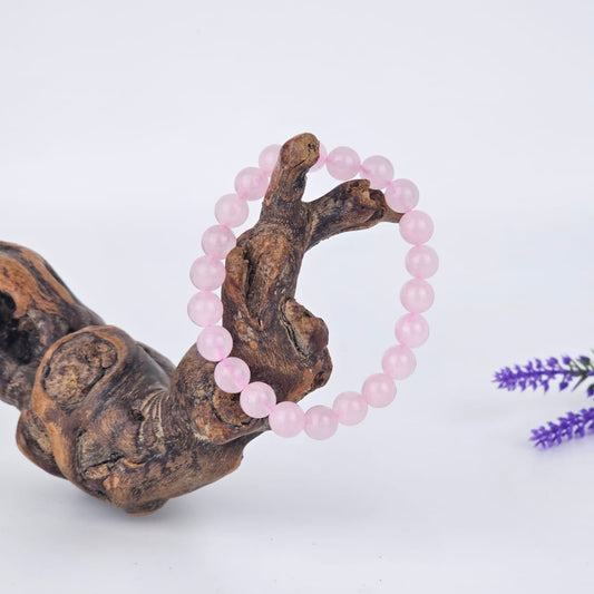 Rose quartz beaded bracelet on a wooden branch, with a white background