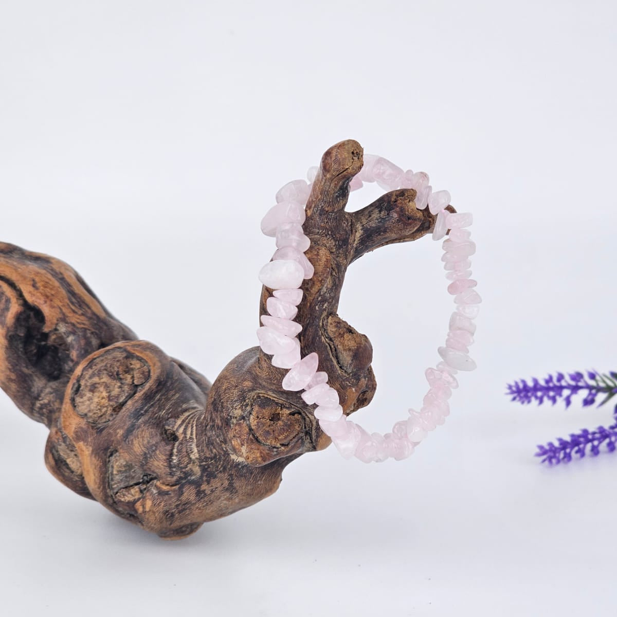 Rose quartz chip bracelet on a wooden branch with a white background