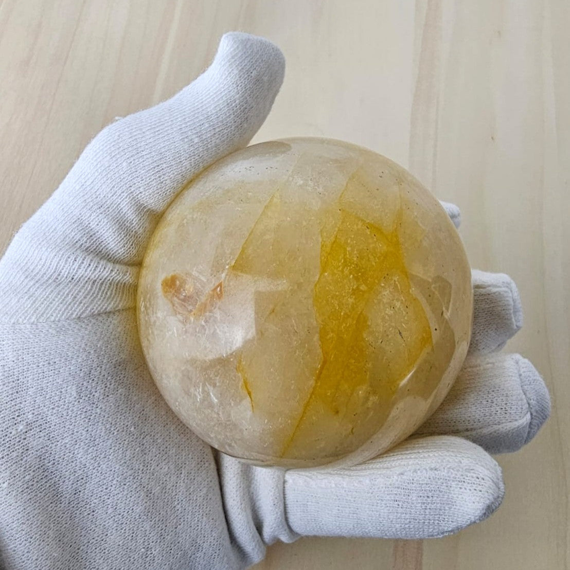 Crystal golden healer sphere with yellow vein held by a gloved hand on a light wooden background