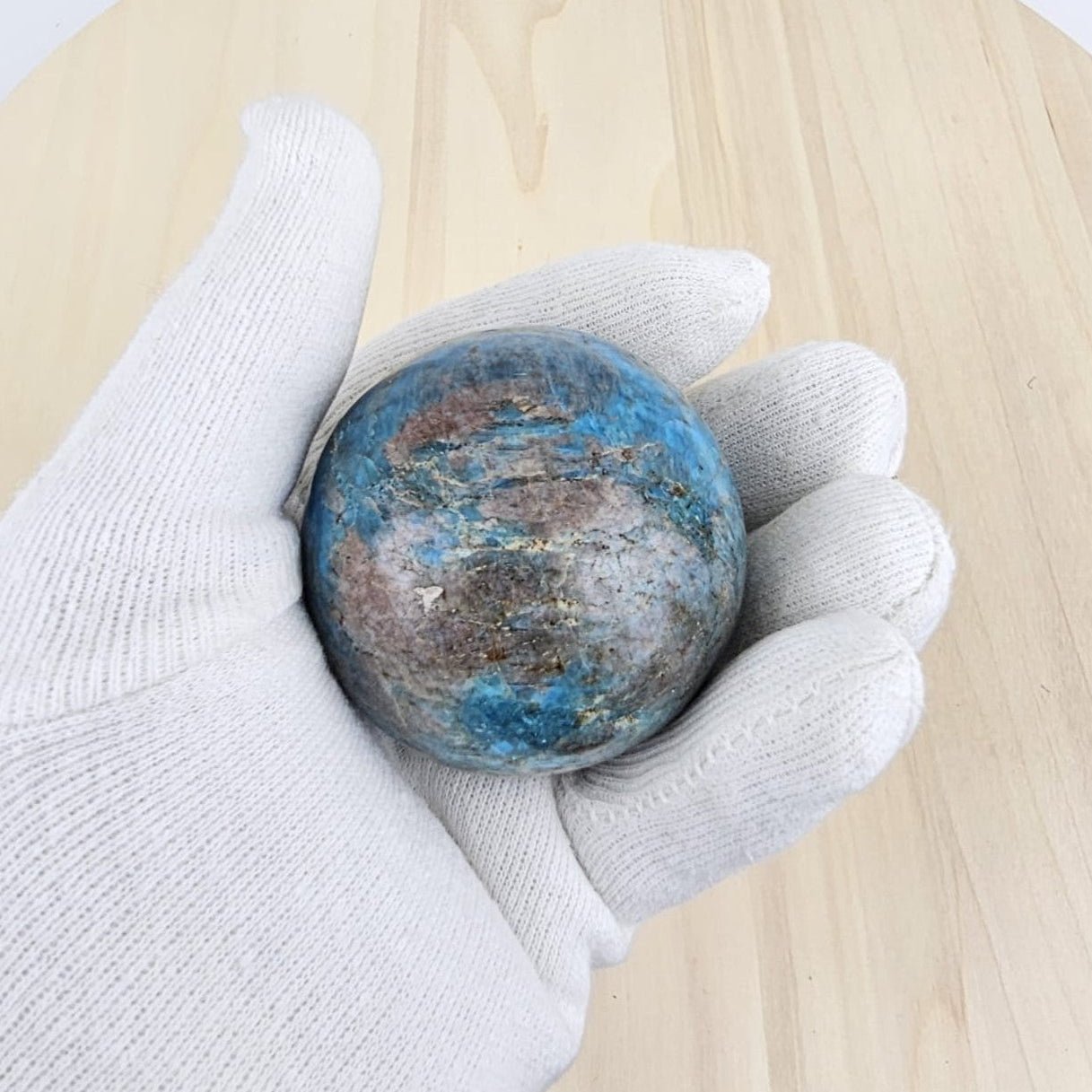 Hand wearing a white glove holding a blue apatite stone on a wooden surface