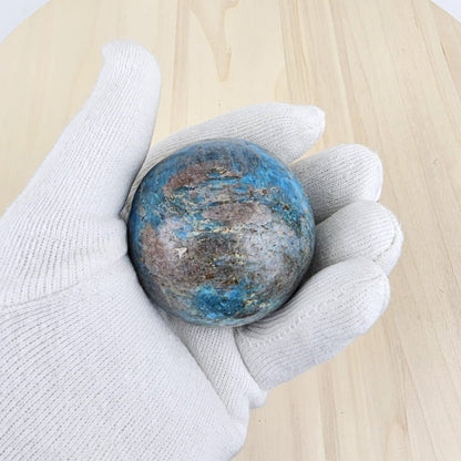 Hand wearing a white glove holding a blue apatite stone on a wooden surface
