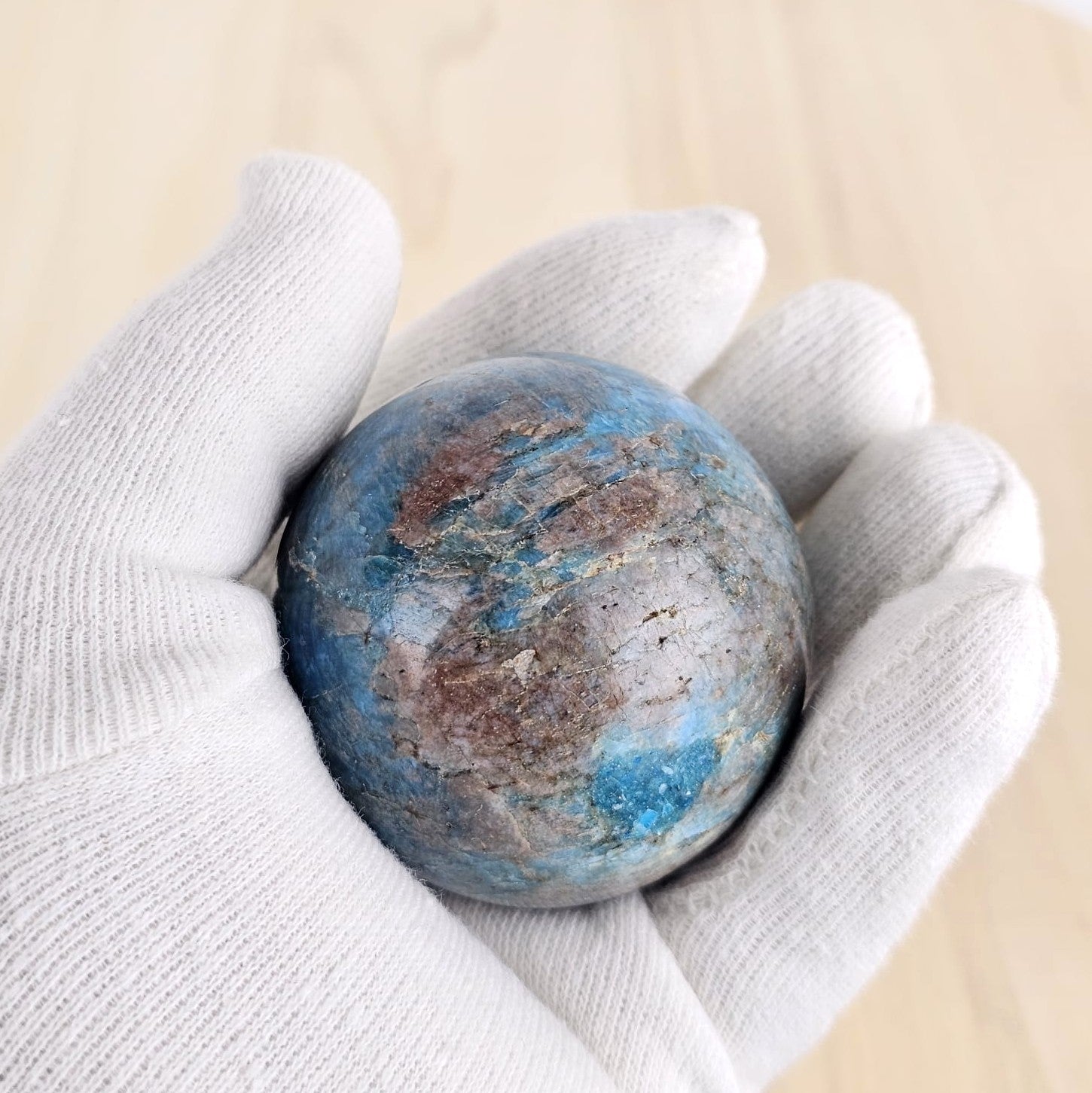 blue apatite crystal sphere in gloved hand on a wooden background