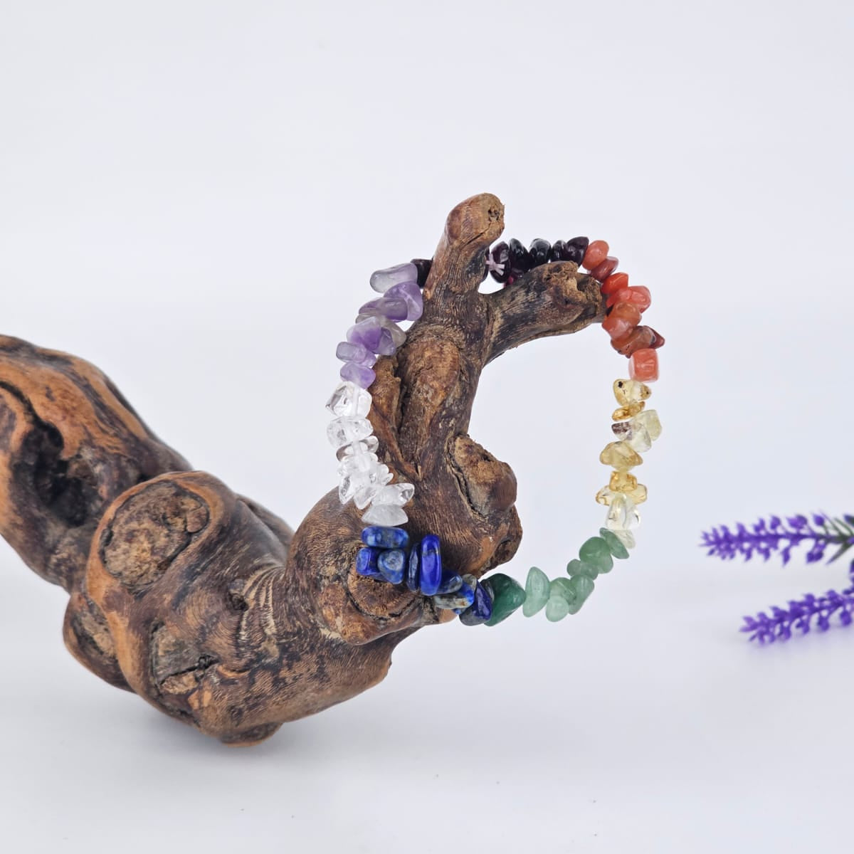 Chakra chip bracelet on a piece of driftwood with a white background.