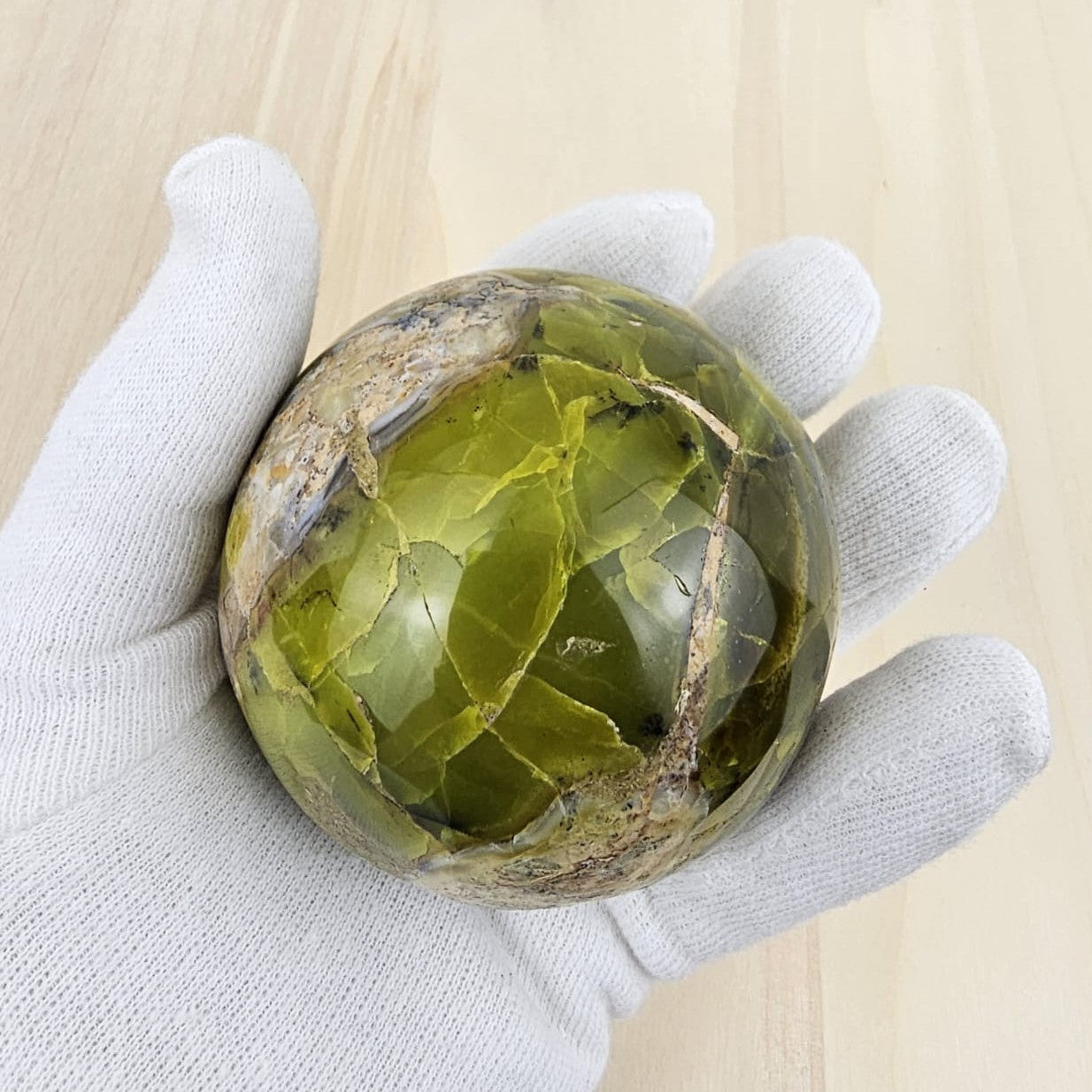 Green opal sphere held by a gloved hand on a light wooden surface