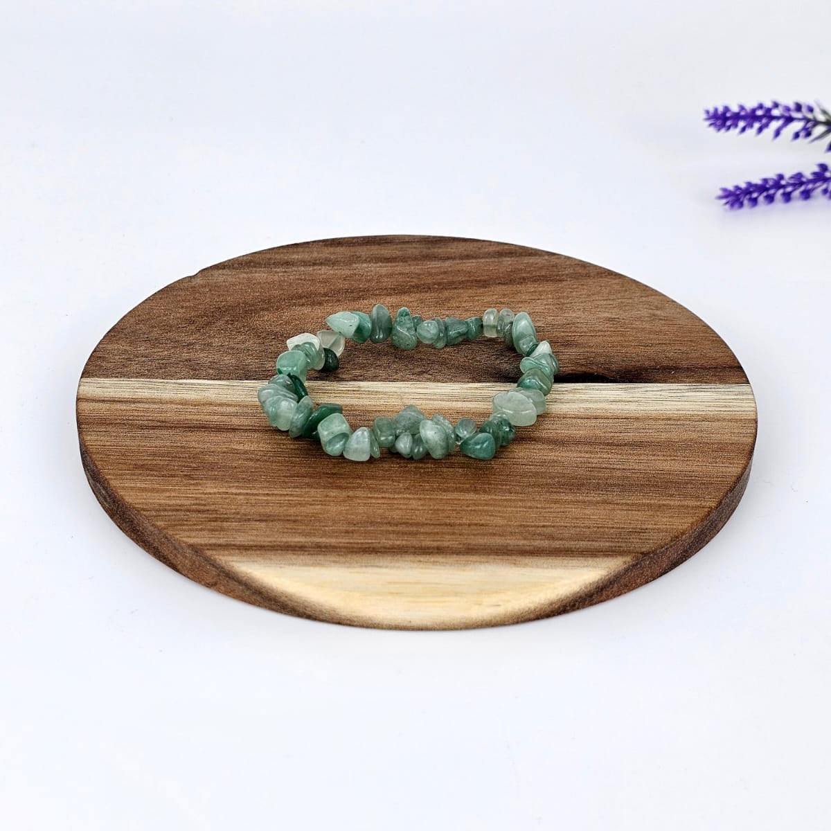 Green aventurine chip bracelet on a wooden plate and a white background
