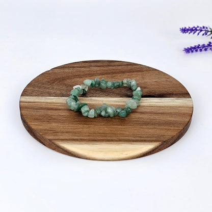 Green aventurine chip bracelet on a wooden plate and a white background