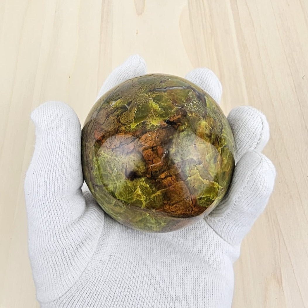 green opal crystal sphere in gloved hand and wooden background