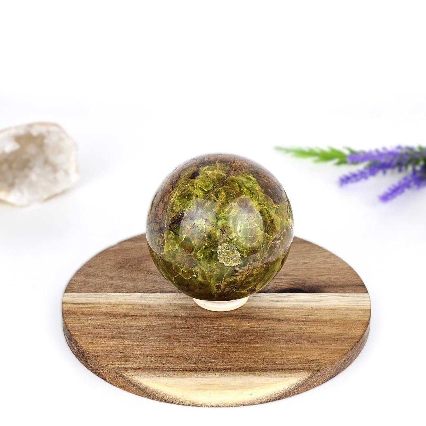 green opal sphere crystal on a wooden plate and white background with purple flower