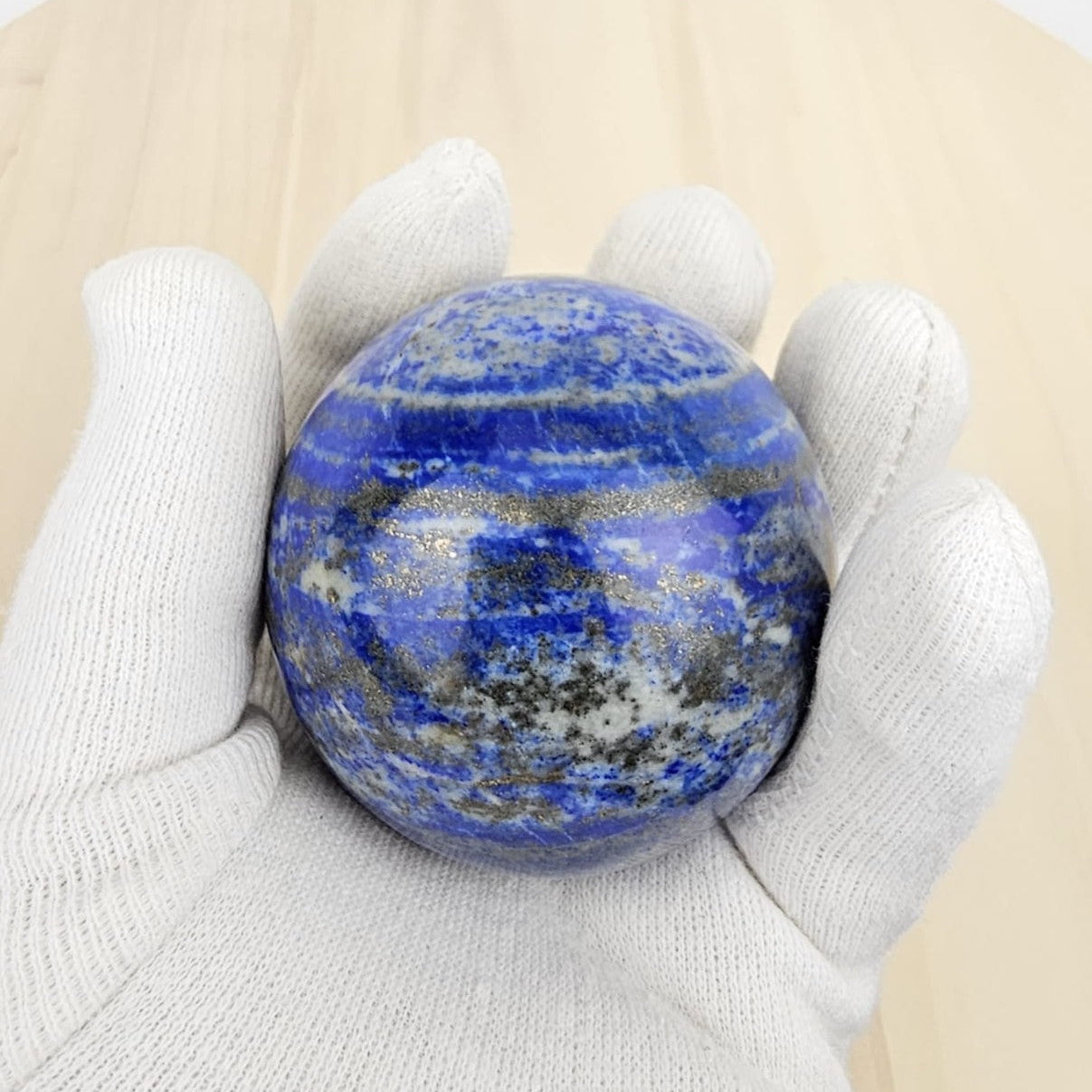 lapis lazuli crystal sphere held in a white glove against a beige background