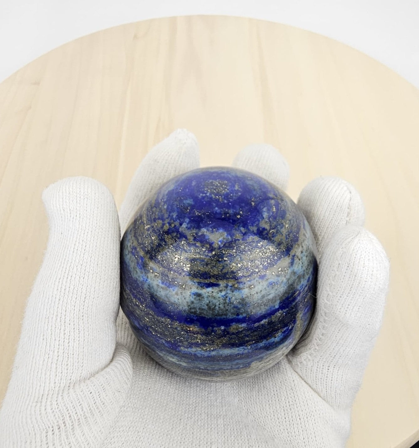lapis lazuli crystal sphere in a white gloved hand on a beige surface
