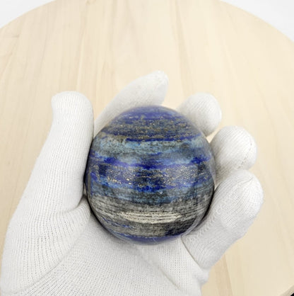 lapis lazuli sphere crystal held in a white glove against a beige background