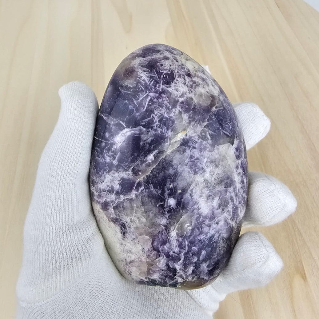 Hand holding a lepidolite stone with white veins on a wooden surface