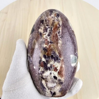 lepidolite in permatite freeform in a gloved hand and a wooden background