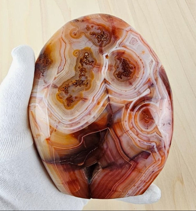 carnelian stone held by a gloved hand on a light wooden background