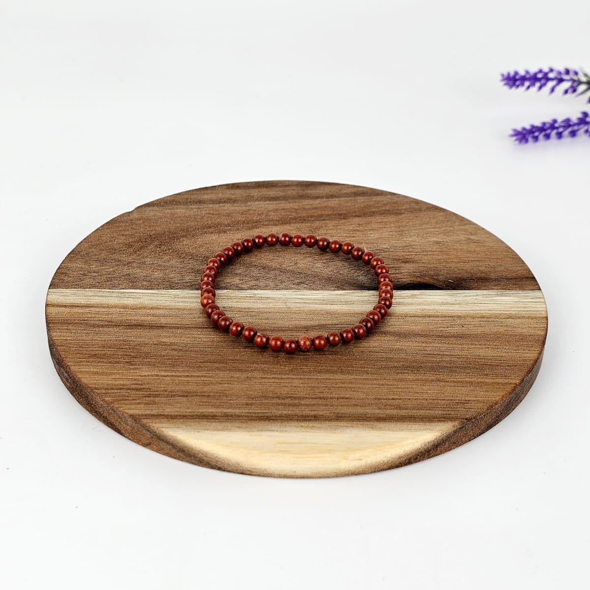Wooden round tray with a red jasper beaded bracelet on a white background