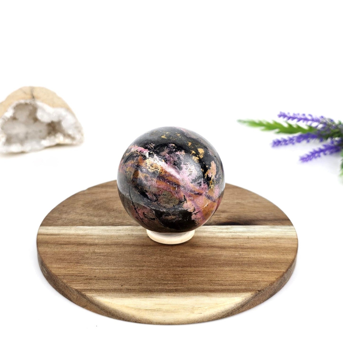 Rhodonite crystal sphere on a wooden plate with a white background