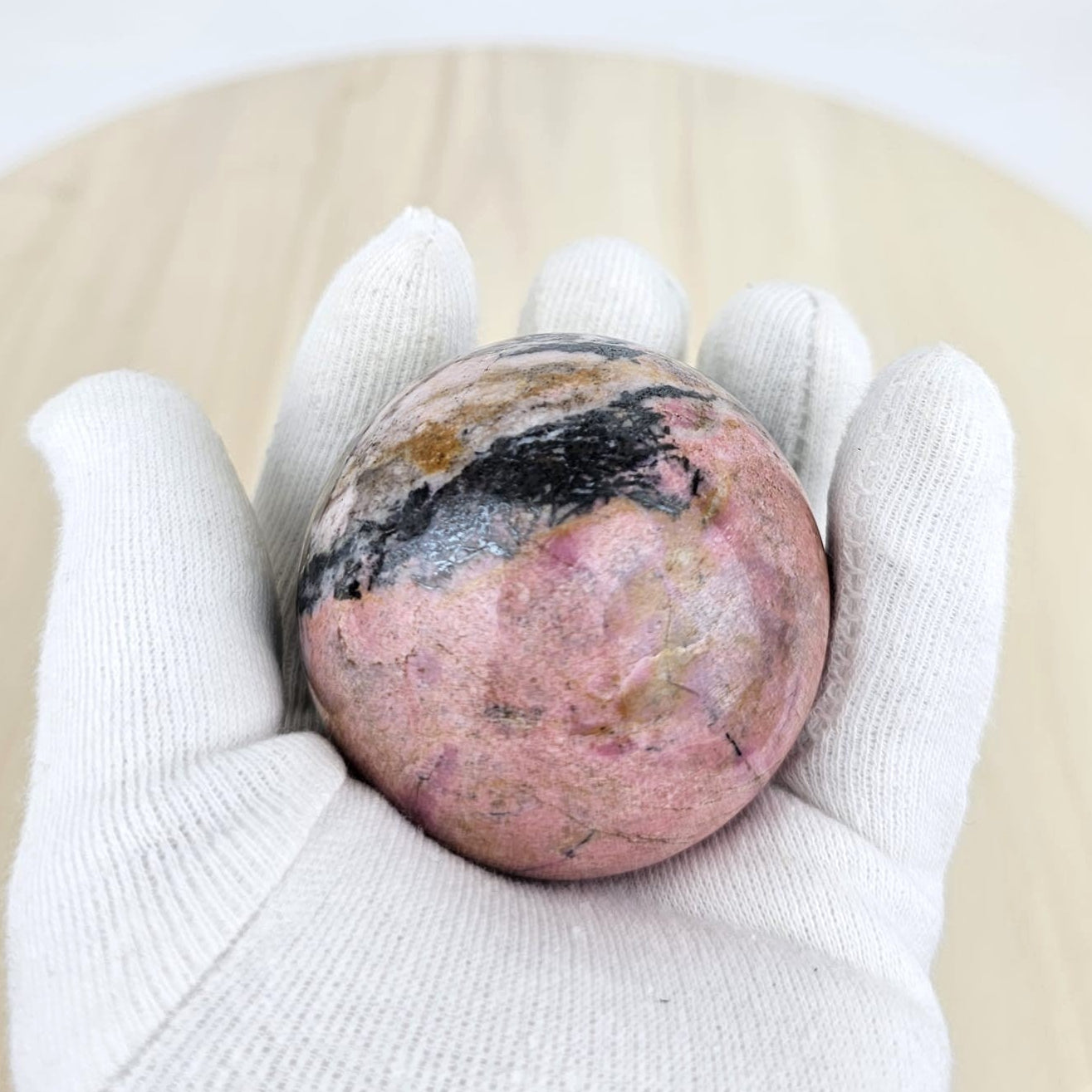 Rhodonite crystal sphere in gloved hand