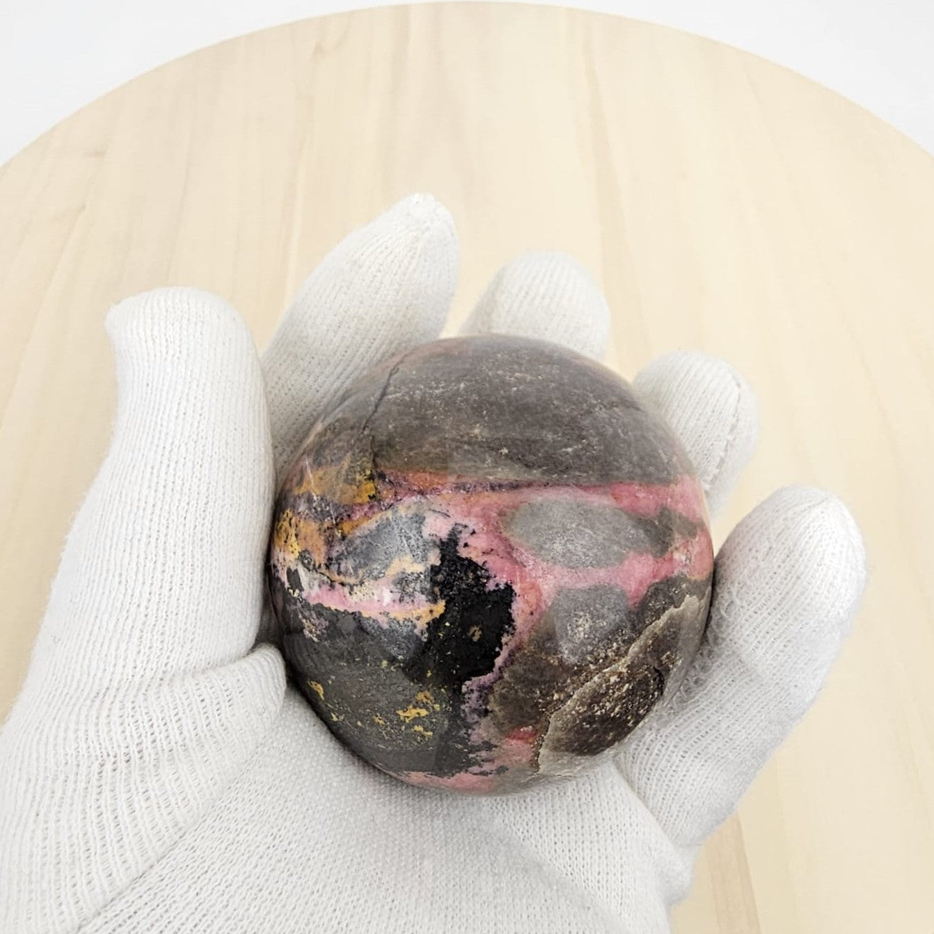 hand holding a rhodonite crystal sphere with a white glove on a beige background